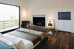 A double bed in a bedroom with dark parquet and a rustic fireplace next to floor-to-ceiling windows