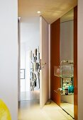 A designer glass wash basin with a shelf in front of a floor-to-ceiling mirror and an open bathroom door