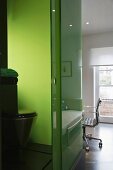 A view into a bathroom with a toilet against a green glass wall