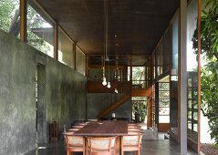 Dining table and traditional chairs with rattan backs in contemporary concrete living space next to ceiling-height terrace doors
