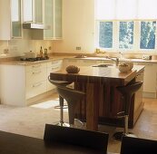 An open-plan kitchen with a free-standing, wooden breakfast bar and designer bar stools