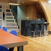 An open-plan kitchen with a black stone bar and designer bar stools