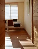 Blick durch offene Tür auf modernem Schreibtisch und Stuhl im schlichten Raum