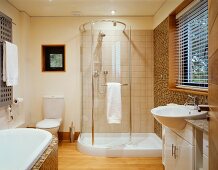 A spacious bathroom with a curved glass shower door and a washstand in front of a window