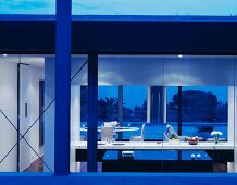 A contemporary house by night with a view through a window in an illuminated kitchen