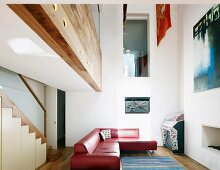 Red leather corner sofa beneath gallery, wall opening with glass balustrade and staircase
