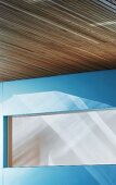 Detail of wood-clad ceiling and opaque window in blue wall