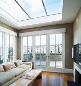 Light sofa and wooden coffee table under glass ceiling and next to terrace doors