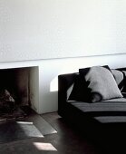 Dezent in weiss und pastellgrau gemustertes Wandpaneel über offener Feuerstelle neben schwarzem, modernen Sofa
