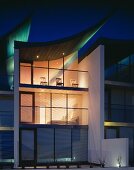 Modern building with illuminated glass facade at dusk and sail-shaped, curving roof with green lighting