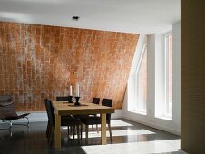 Solid wooden table with leather-upholstered chairs and a modern leather armchair in front of a brick-clad sloping ceiling