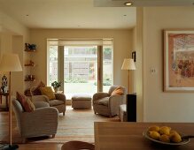 Grey armchairs with scatter cushions and Scandinavian-style standard lamps in open-plan living-dining room with large windows