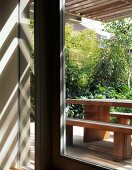 Sunbeams through wooden pergola above garden terrace with simple seating made from heavy wooden boards