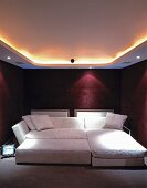 Indirect ceiling light and spotlights above a wide sofa bed in bordeaux-coloured bedroom