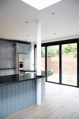 A kitchen in a country house with a pillar integrated into a curved bar in front of floor-to-ceiling windows