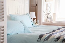 Double bed with light blue pillows and bedspread near a window
