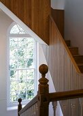 Traditional stairwell with arched window and modern wooden stairs with solid balustrade