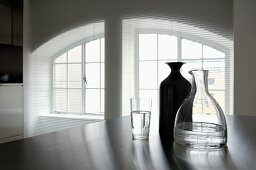 Offene Jalousie vor geteilter Fensterfront mit Segmentbogen, Karaffen und Wasserglas im Vordergrund