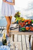 A woman on a jetty with vegetables and champagne