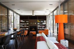 Open-plan dining and living room with orange standard lamp in front of floor-to-ceiling windows with closed blinds