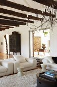 Ethnic style in spacious house - simple, modern sofa set and romantic chandelier below ceiling beams of unworked logs