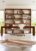 Office area flooded with light with long desk and two swivel chairs in front of open wooden shelving