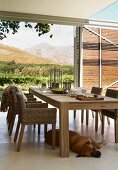 Holzstühle mit Geflecht zu handwerklich gearbeitetem, modernem Holztisch auf dem überdachtem Essplatz mit grossartigem Landschaftsblick