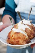 A person holding a plate of jacket potatoes with sour cream
