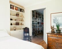 Modernes Bett und Antiquitäten neben offener Tür mit Blick auf moderne Bücherwand