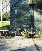Sonniger Terrassenplatz mit Natursteinwand und Metallmöbeln auf alten Steinplatten