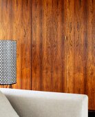 Detail of sofa arm and standard lamp in front of cupboard with wooden doors