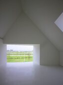 Empty, modern attic room with frameless, glazed wall aperture and view of landscape