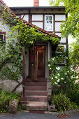 Old half-timbered house with steps leading to climber-covered front door