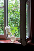 White roses in glass jug in front of open window with view of garden