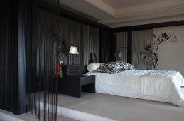 Elegant bedroom with black bamboo canes and thread curtains against walls around bed with white covers