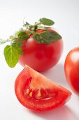 A slice of tomato and a whole tomato with leaves