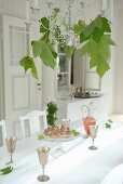 Silber Weinbecher auf weißem Tischtuch und Deckenkerzenleuchter mit Platanenblättern dekoriert in weißem Zimmer im Landhausstil