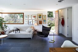 Indirect lighting and slate-flagged floor in modern living room with long corner window and open front door