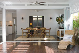 Rattan lounger on modern terrace in front of open-plan living-dining room with view of rustic wooden chairs around table