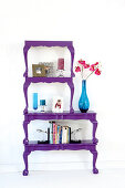 Books and blue glass vases on antique-style tables halved, painted purple and stacked to make decorative shelves