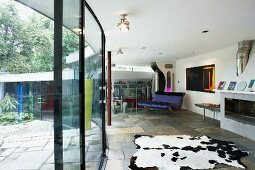Curved glass wall on stone floor between terrace and modern living space with cow skin rug and rocking sofa