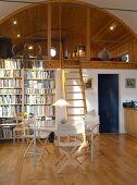 Essplatz mit Bücherregal neben Leiter zu gemütlicher Schlafgalerie mit holzverkleidetem Tonnengewölbe