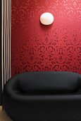 Schwarzes Designersofa vor roter Tapete mit traditionellem, floralem Muster
