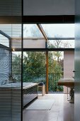Modern bathroom in solar house with view of sky and trees through glass wall with sliding element and glass roof