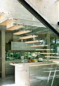 Open wooden staircase with glass stringer and steel girder in front of concrete kitchen in contemporary solar house