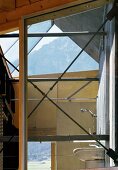 View of bathroom through steel struts on window of modern wooden house with view of mountains
