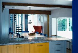 View of dining area with fifties chairs across modern kitchen unit with colourful wooden fronts and granite counter