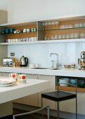 A modern kitchen with a crockery shelf and a bar with a bar stool