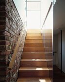 Modern wooden staircase with handrail on brick wall