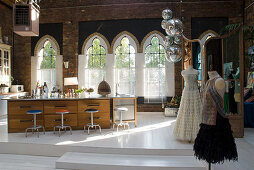 Large, free-standing kitchen island and tailor's dummies wearing elegant gowns in brick loft with church windows
